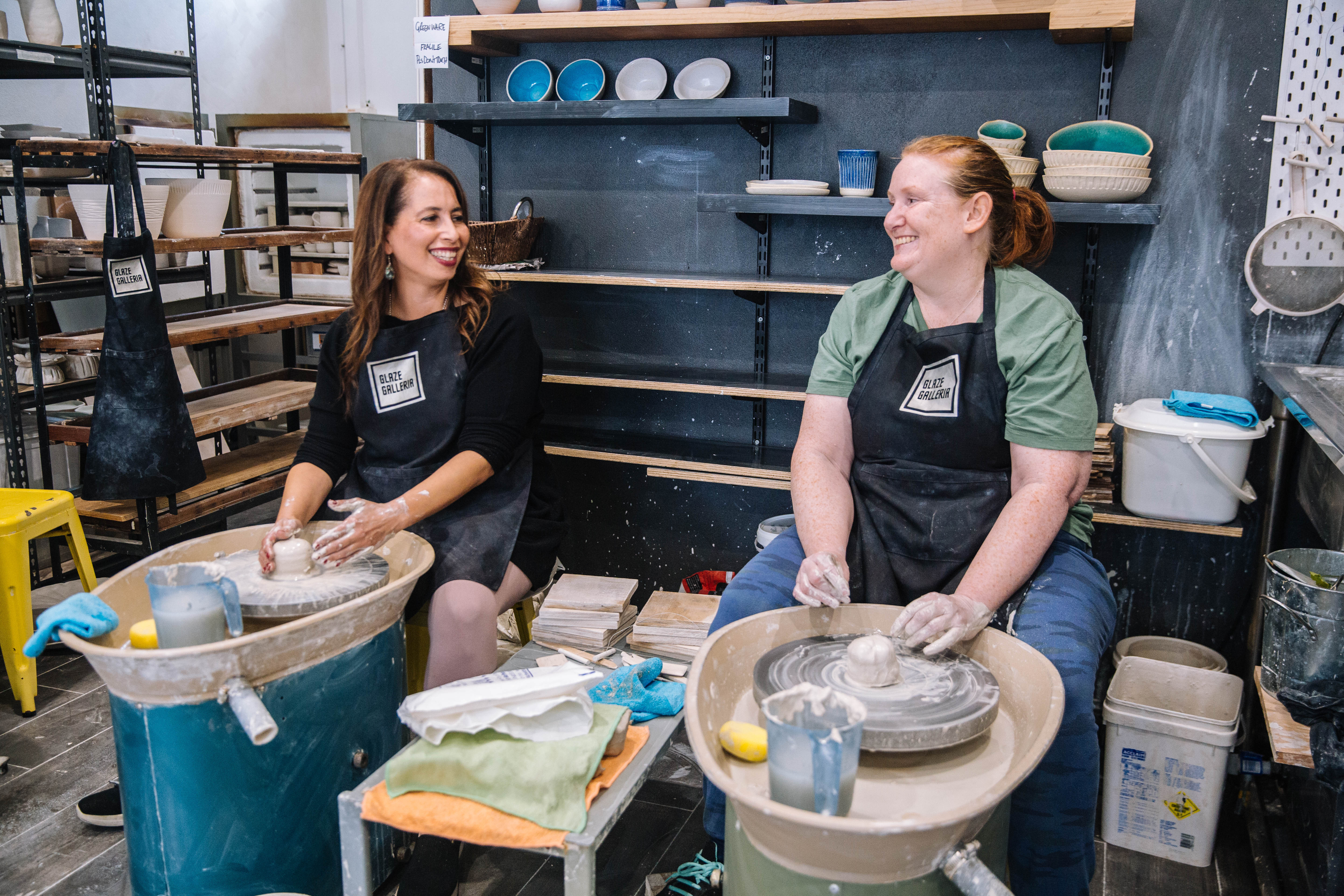 Two women sit side by side at a pottery class